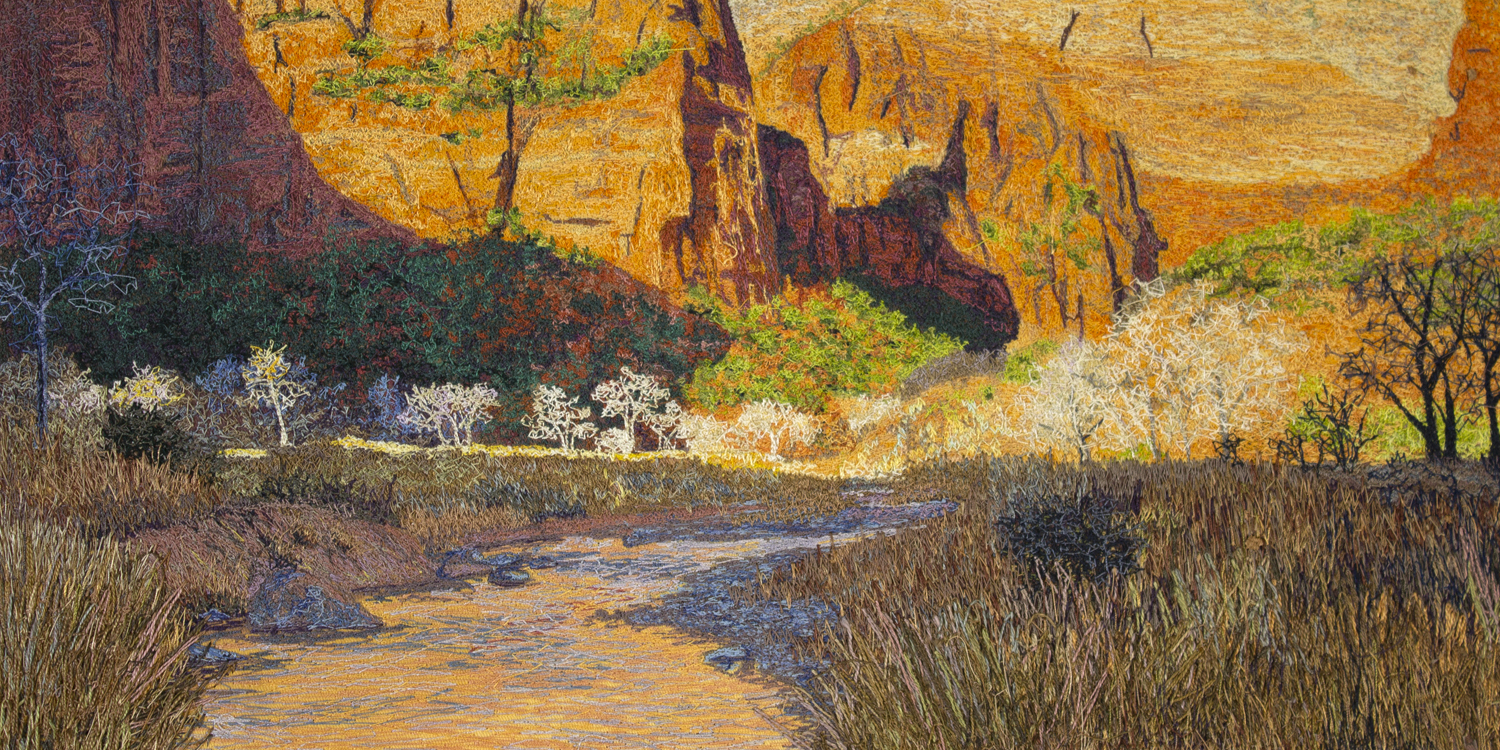 An image created using colored thread and fabric. In the foreground, a shallow river flows between rocky banks of dry grass and dirt. In the middleground, leafless cottonwood trees are illuminated by the warm sun. In the background, green slopes build up to tall sandstone cliffs. These yellow-orange sandstone cliffs form the backdrop of the image.