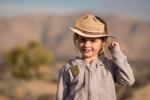 A young female child stands with her pin and a paper cutout Park Ranger hat
