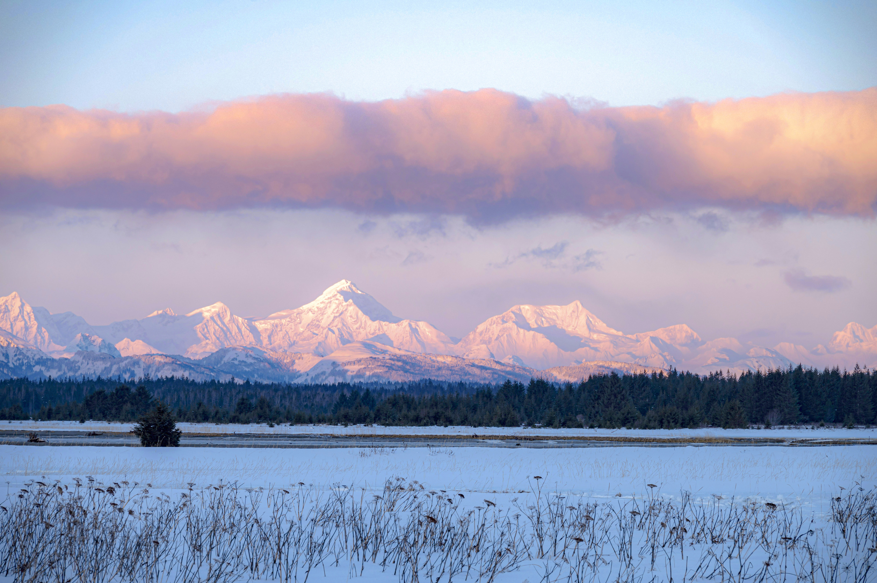 Sunrise turns clouds and mountains shades of pink and orange in a wintry scene.