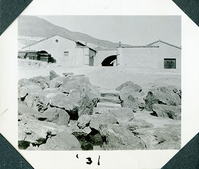 This is an historic black and white photograph from the Scotty's Castle Historic Photograph Collection, Death Valley National Park of Scotty's Castle Watercourse showing east end steps with Stables in background. 1931.