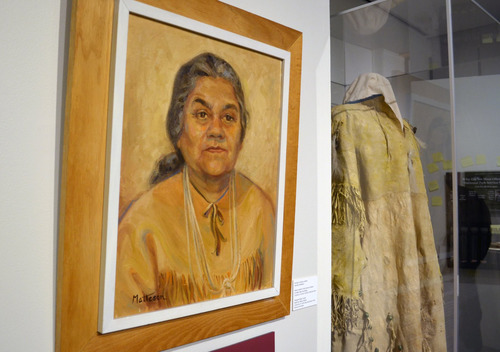 A portrait of a woman in American Indian attire hangs on a wall next to a clear case containing the actual outfit
