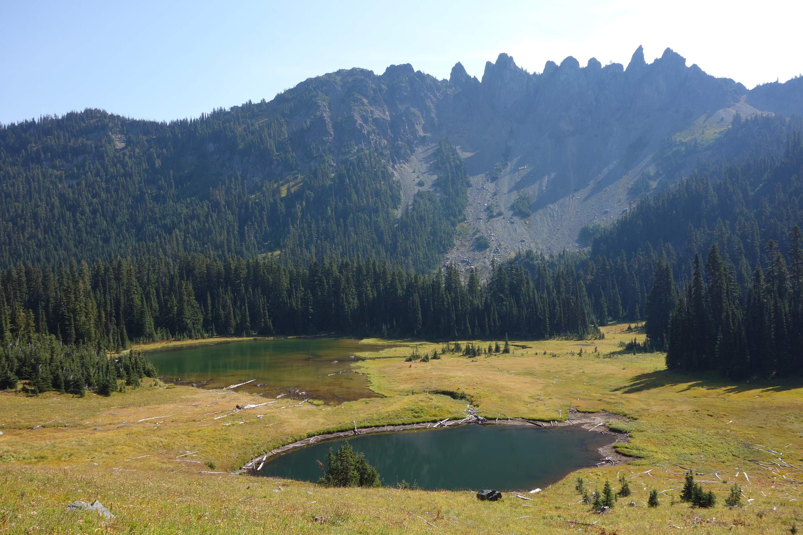 Two small lakes in a subalpine valley underneath a rocky ridgeline. 
