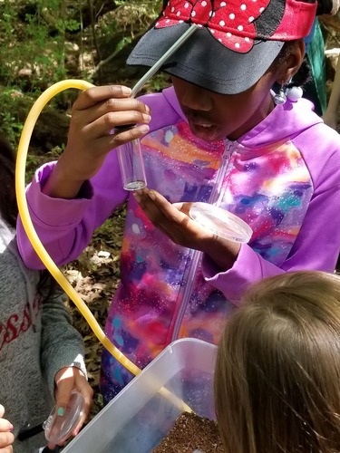 A young girl holds a vial with a tube coming out the top in her right hand, while looking intently at the bottom of the vial.