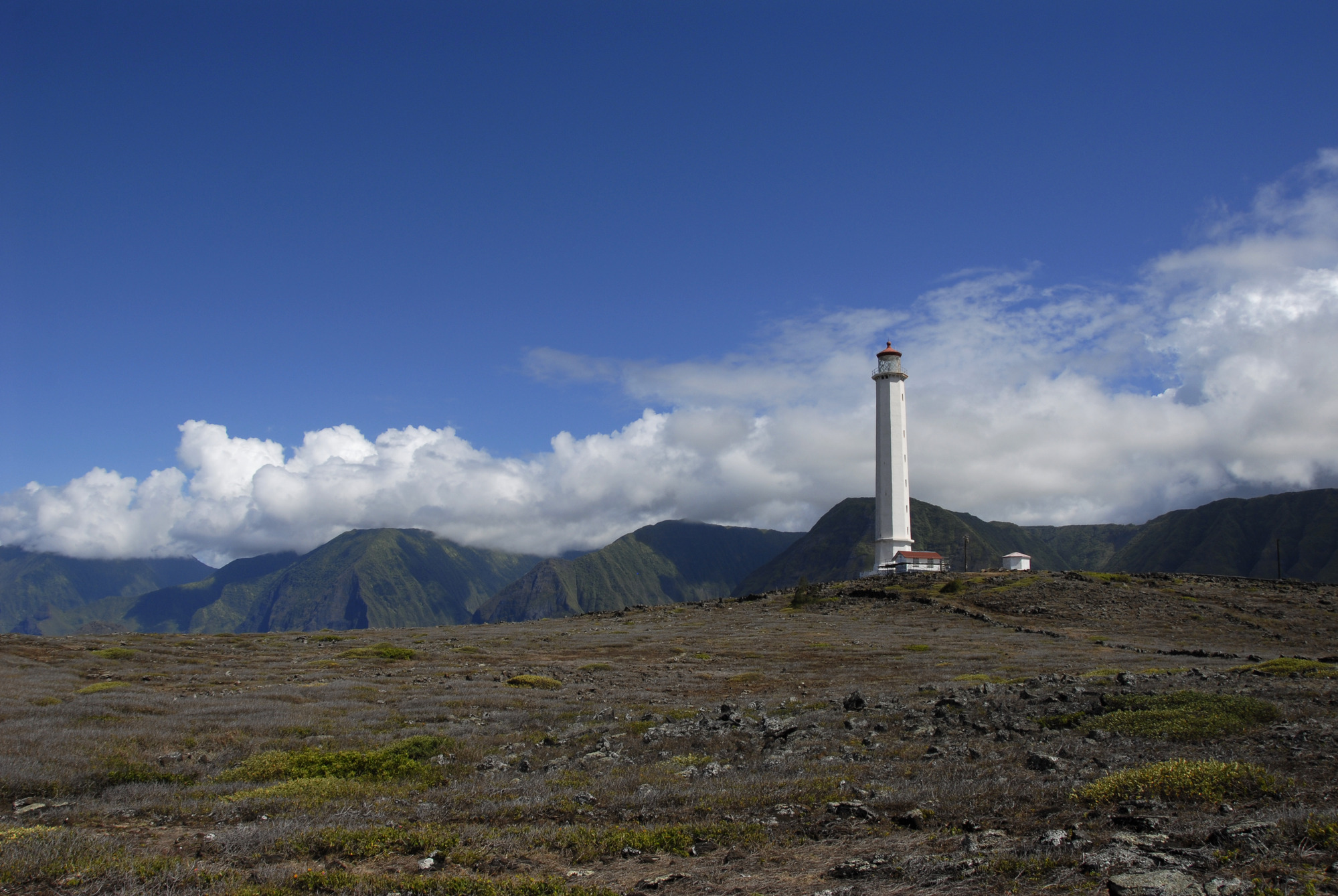 A tall, thin white building on a hill with sea cliffs in the background.