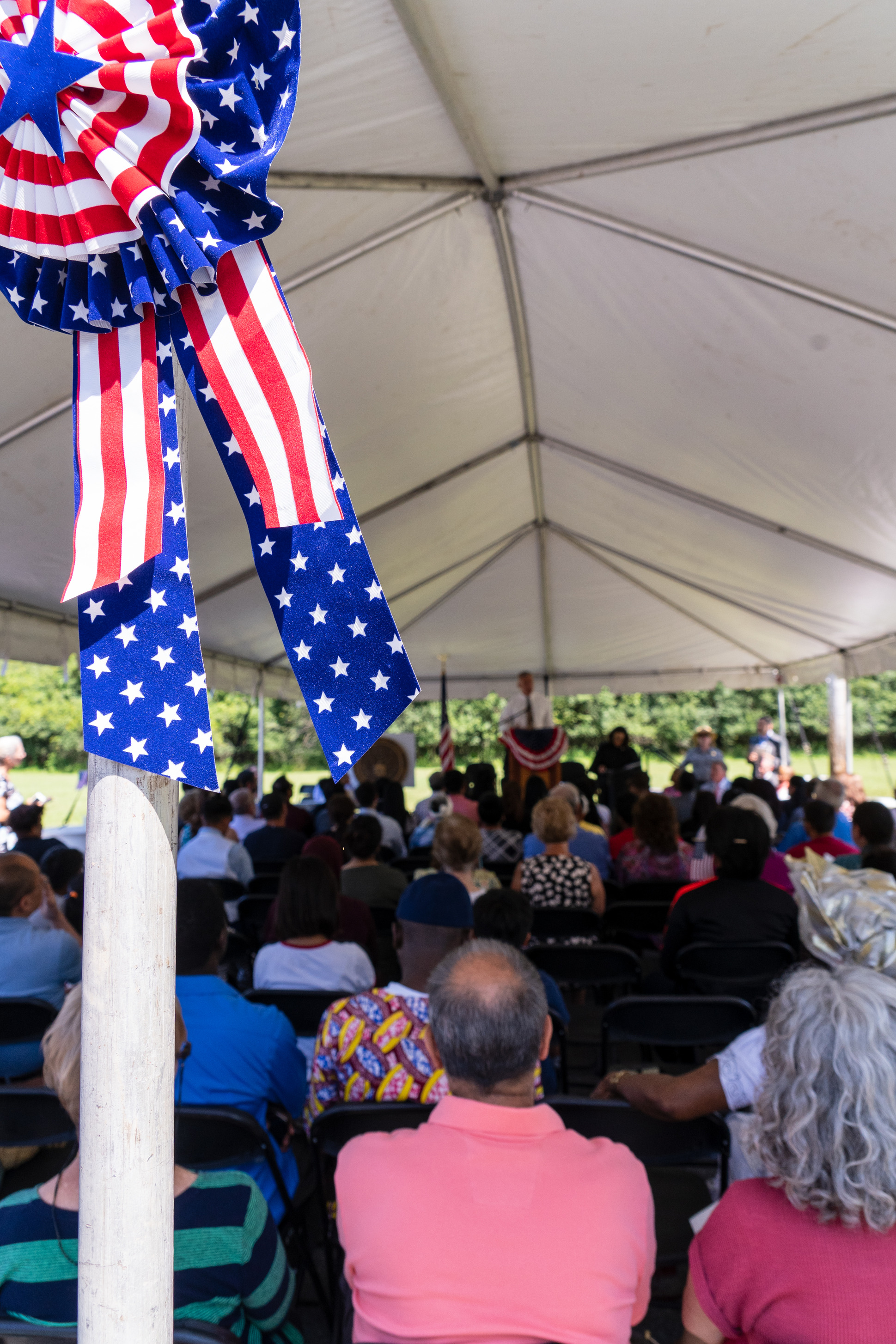 People sit under a tent and listen to a man speak at a podium.