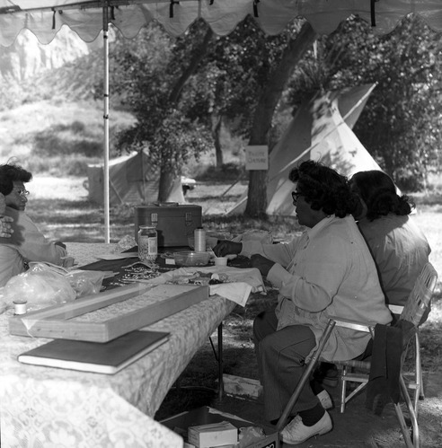 Three women demonstrate beading at first annual Folklife Festival at Zion National Park Nature Center, September 1977. Sign by tipi in background reads: Paiute Culture.