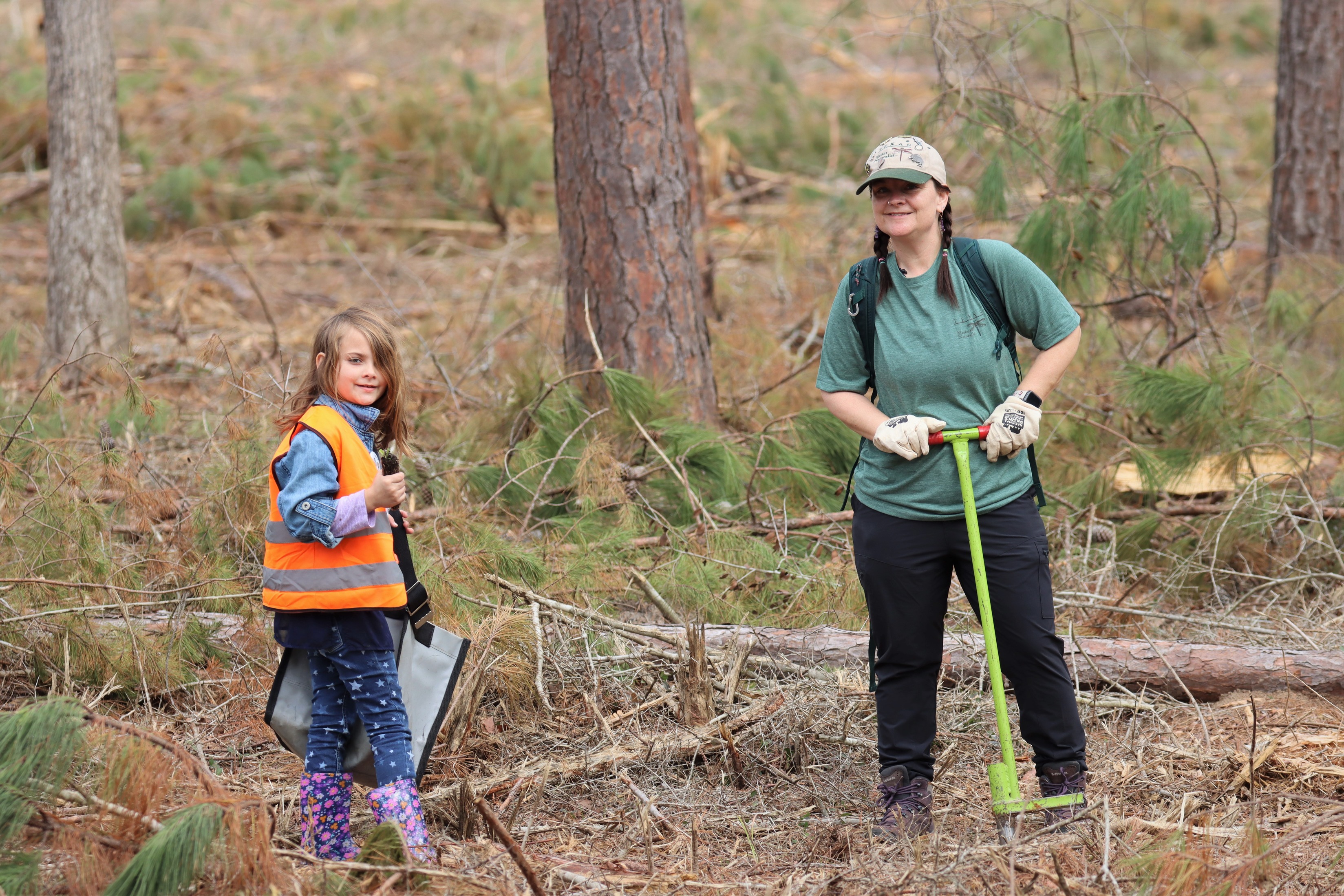 Mother and daughter posing for a photo while planting grasses in an open part of the forest