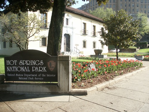 Red tulips in a bed in front of the Hot Springs National Park administration building, next to the park's Bathhouse Row entrance sign