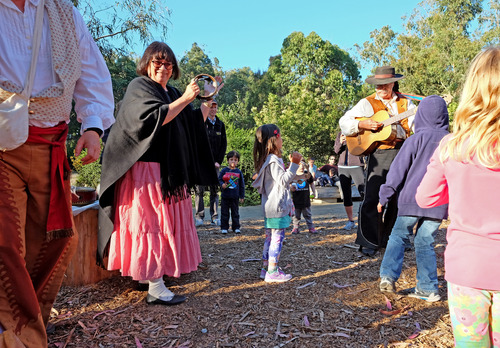 Musicians in colonial dress play the guitar and tambourine at Rob Hill Campground while children watch.