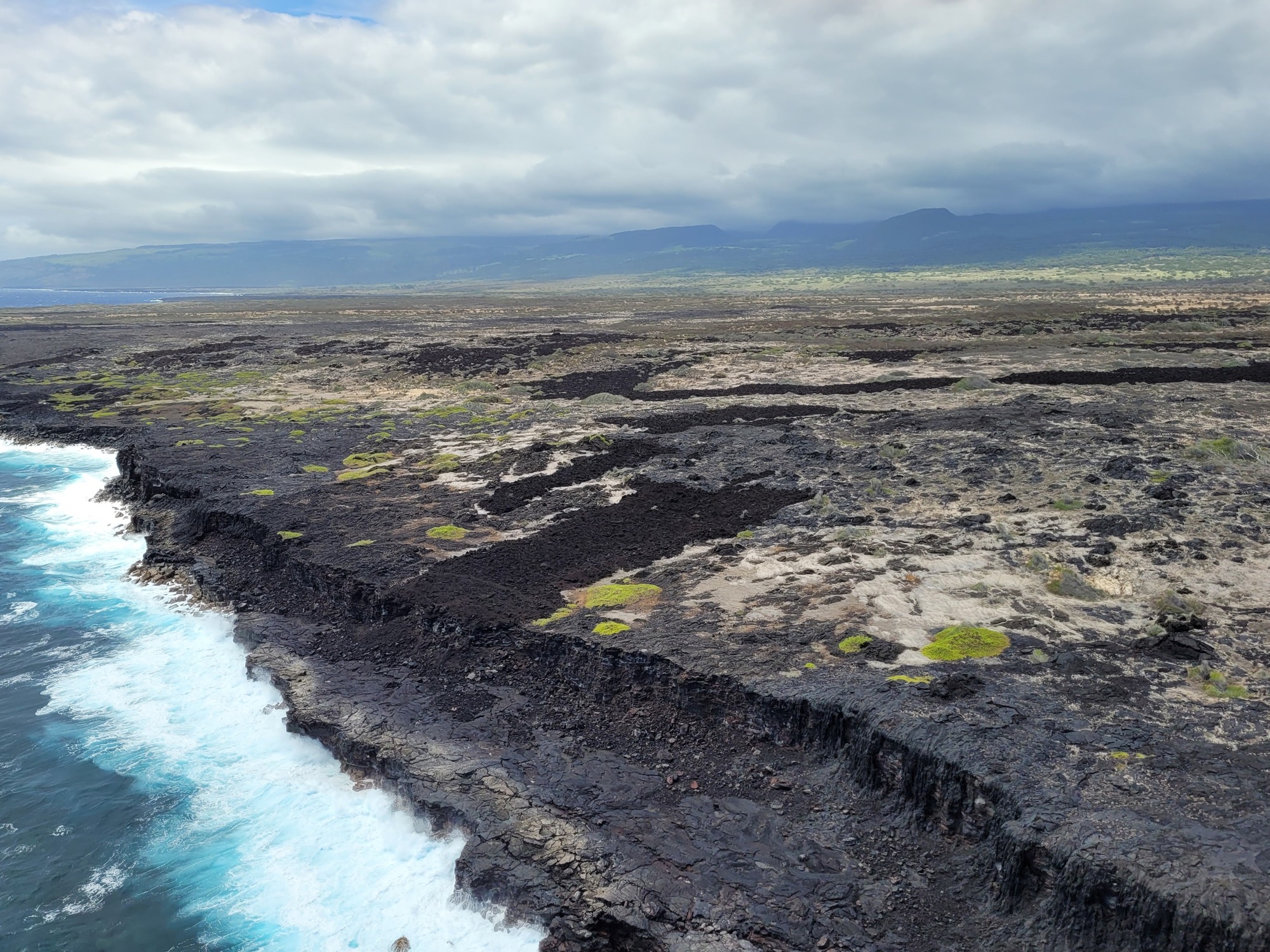 A volcanic coastline with waves crashing along sea cliffs. 