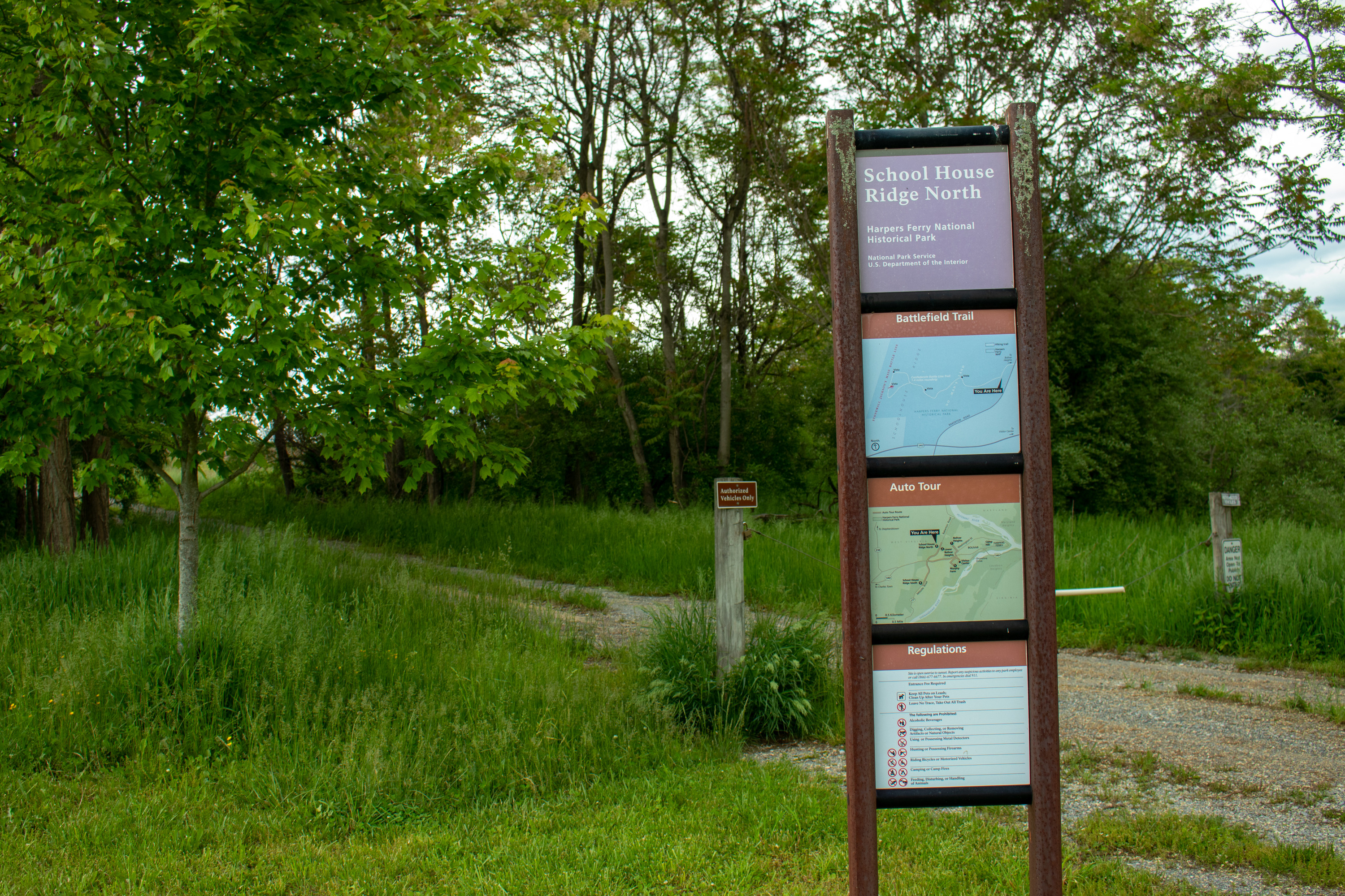 Tall and skinny trail information sign sharing the name and the various trails that you can do while visiting the Schoolhouse Ridge North Property. You can see the start to the walking trail behind the sign.