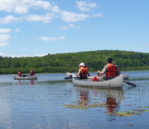People in canoes  on a calm Little Beaver Lake with a tree covered hill in the distance.