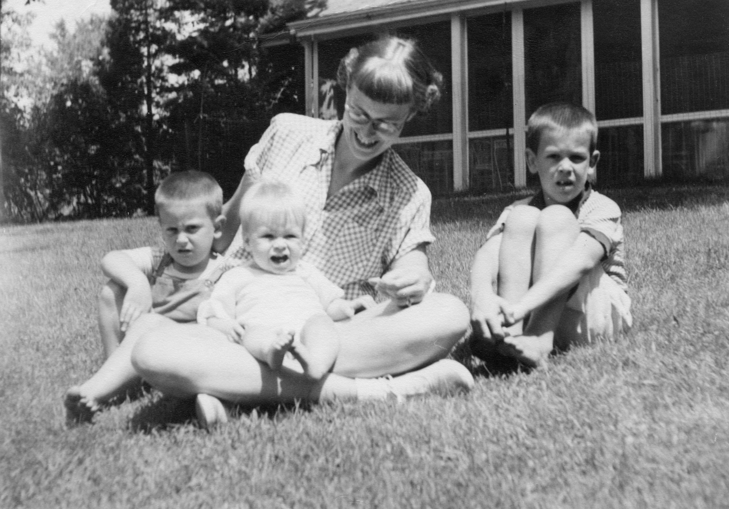 A woman sitting with three children in the grass.