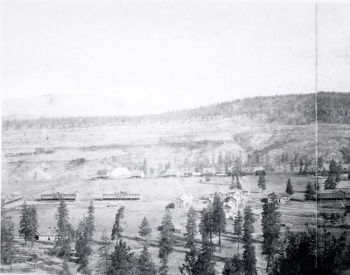 Faded black and white photograph of buildings in a wide forested valley