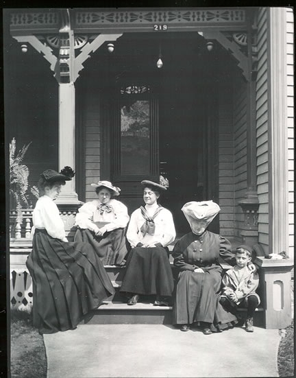 Group of women on front porch of Gates-Wallace home, 219 N. Delaware St., Independence, MO. Bess Wallace is seated second from left. Her youngest brother Fred is also pictured. Negative, HSTR 28928.