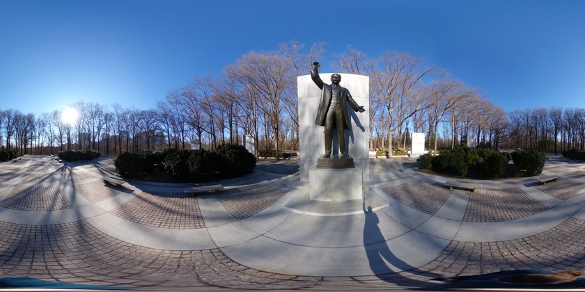 Spherical image of a memorial plaza surrounded with woods. The plaza include a large statue of Theodore Roosevelt, two large fountains ponds, and two bridges over pools.