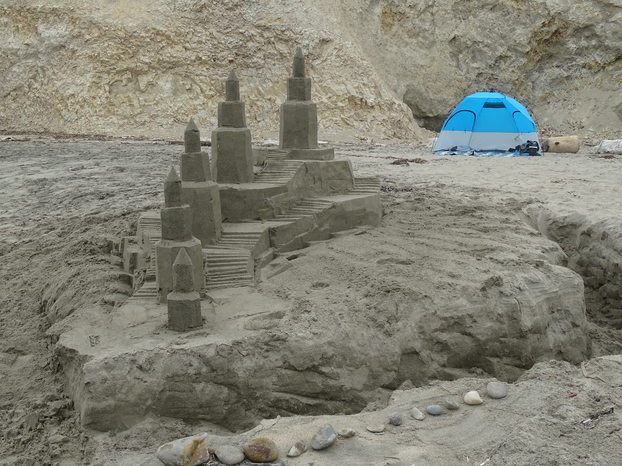 A large sand sculpture of a castle with five octagonally shaped towers and lots of staircases.