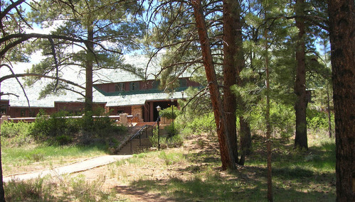The overhanging roof and stone pillars of the large lodge are visible through pine trees.