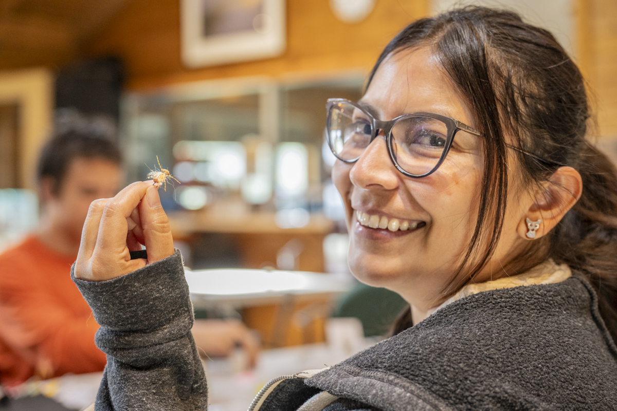 A woman holds up a tiny fishing fly that she tied.