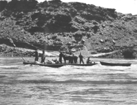 Historic photograph of ferryboat at Lees Ferry. The boat is relatively small. Five people and two horses or mules are on board. The ferry is guided by wires spanning the river.