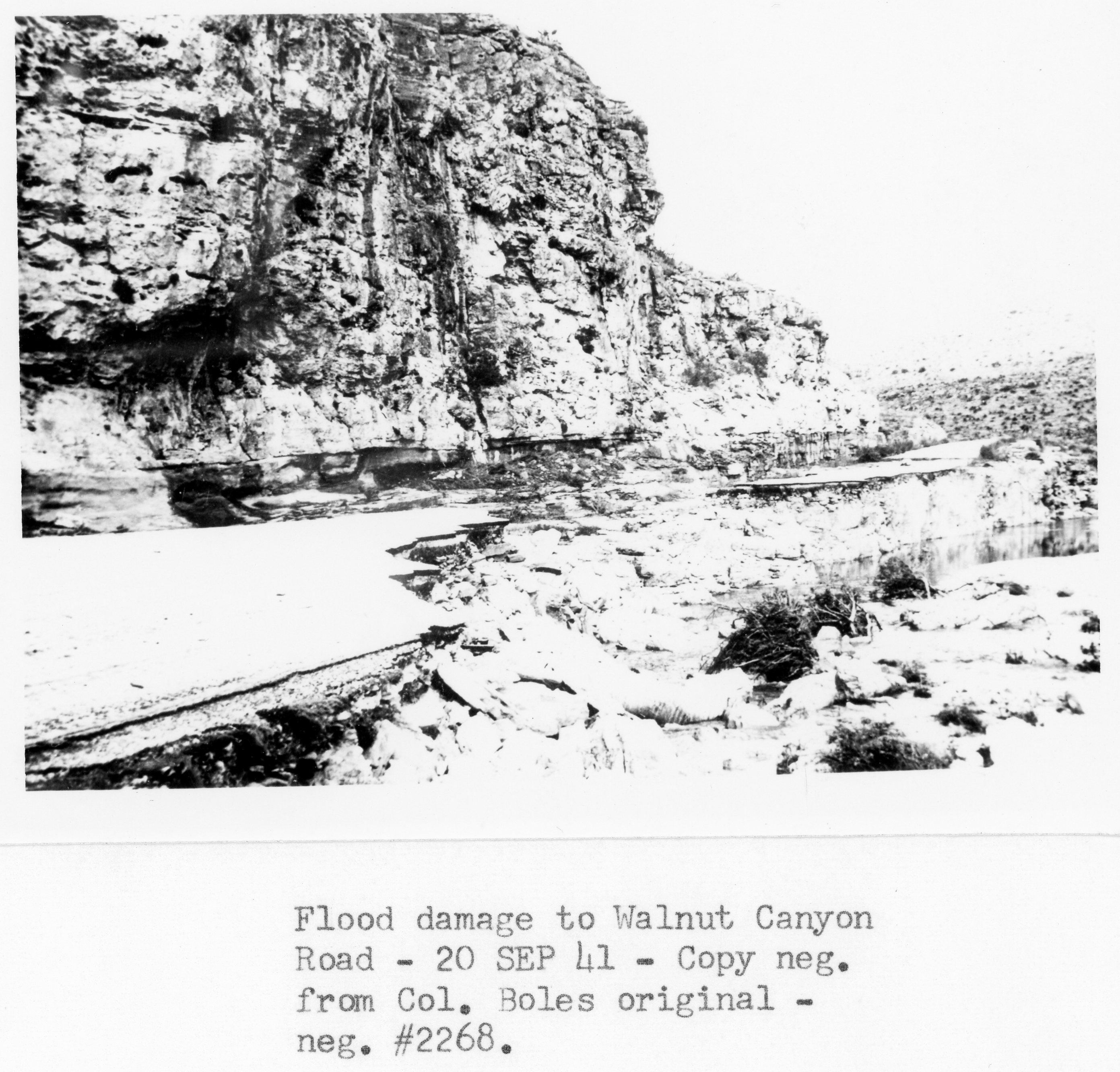 A black and white photograph showing the flood damage to the Walnut Canyon Road.
