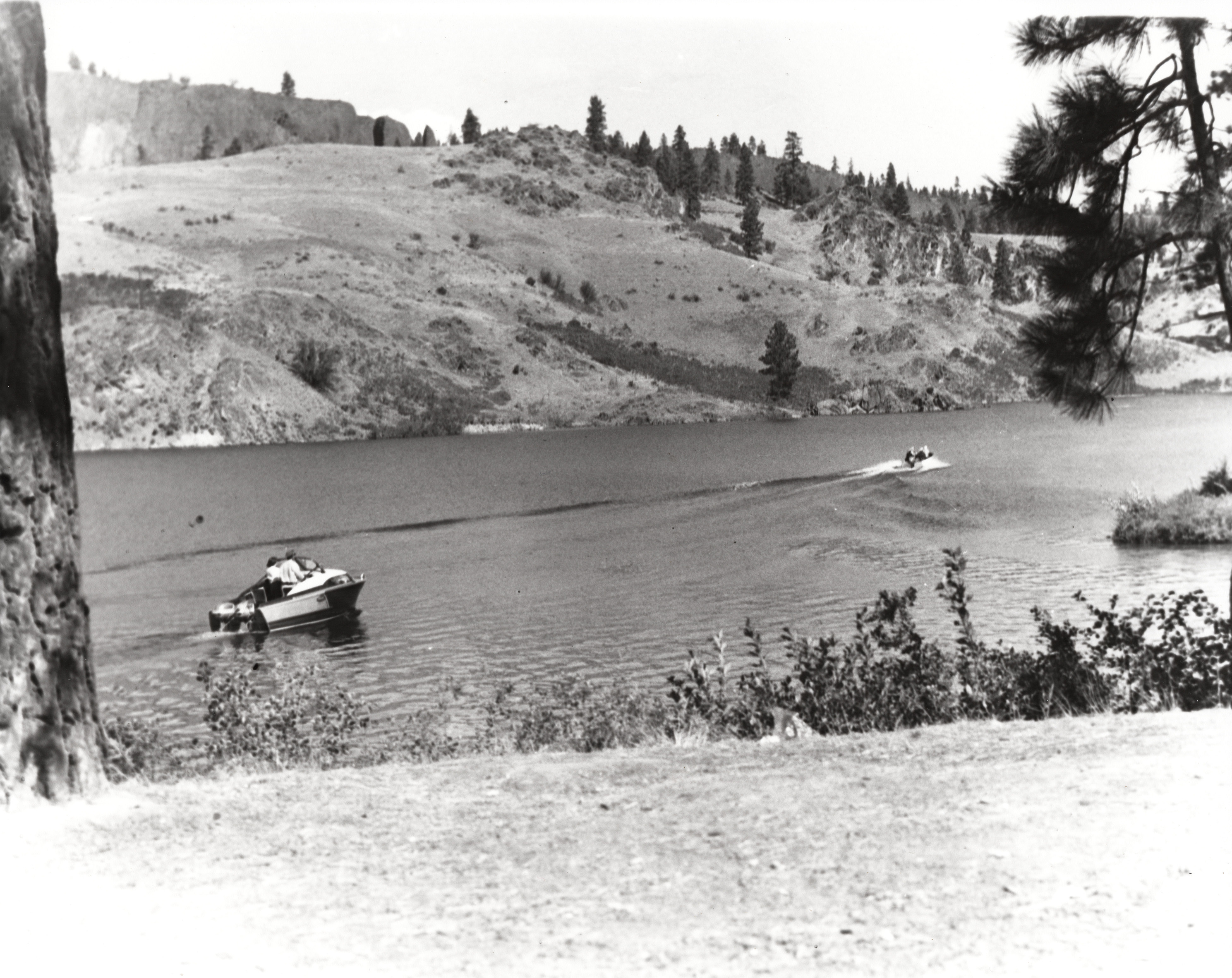 Black and white photograph of two motorboats travelling across a lake