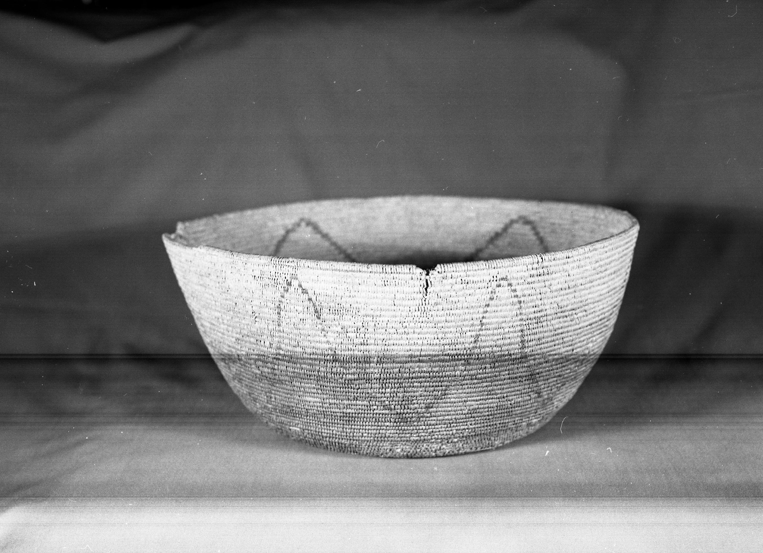 Private Collection. Object: Miwok basket. Dimensions: 15 x 6 1/2". Materials: Bracken fern, redbud, split shoot. Repaired with split shoot. Technology: Base in single rod interlocking stitch. Upper 2/3 basket in three rod coiling, stitched closely spaced redbud used in lower 1/2 design, bracken fern root in upper 1/2. Splices appear to be concealed in foundation. Repair on base in cotton string. Collection History: Probably purchased from Mrs. Mary Longfellow Poncho (Maggie Longfellow Antonini's mother). Photographed by Michael Dixon. Catalogued by Craig Bates and Barbara Beroza. Yosemite Collections, National Park Service.