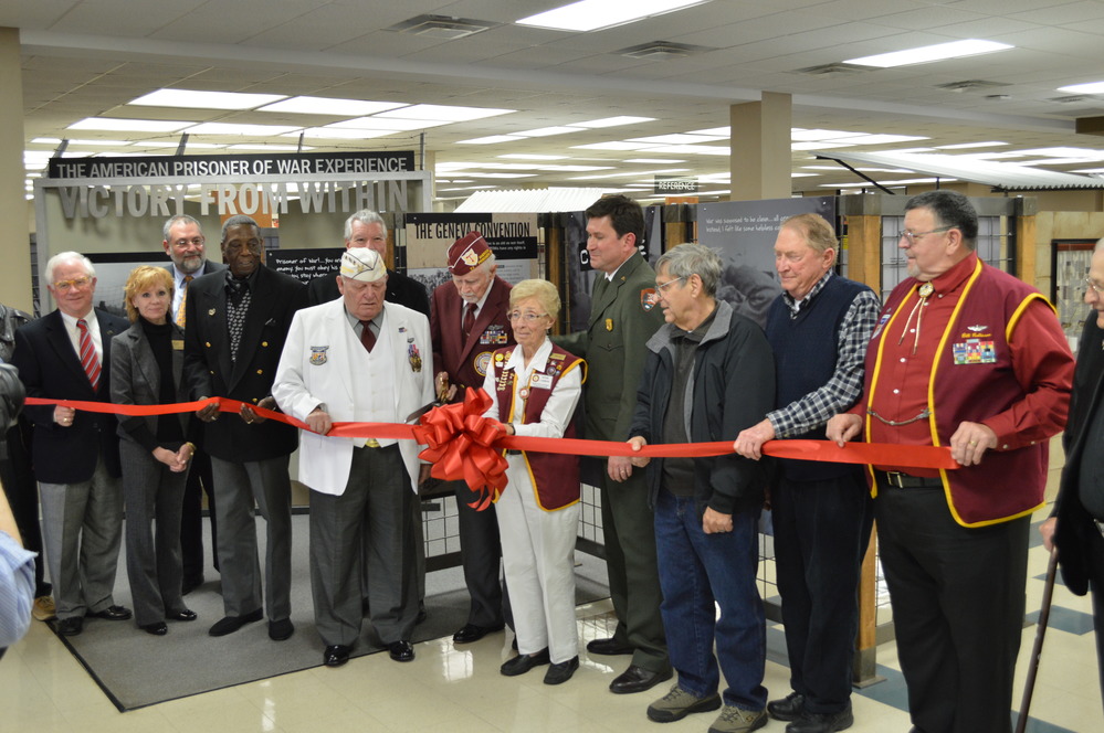 A group stands before exhibits with a red ribbon