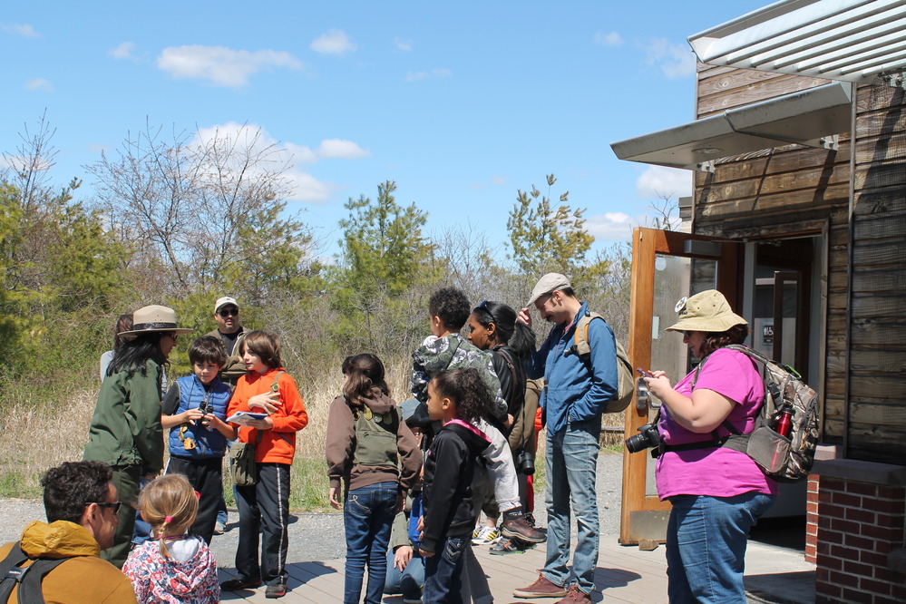 Ranger and junior rangers with family gather outside for a nature hike.
