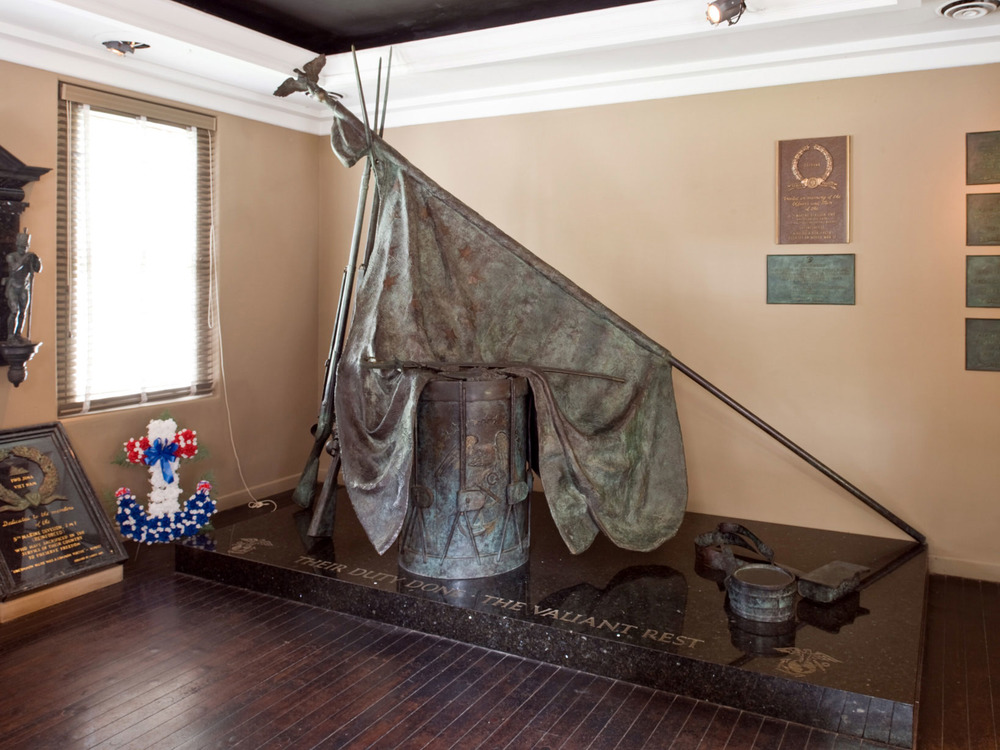 Color photo of a bronze sculpture showing a drum with a flag draped upon it.