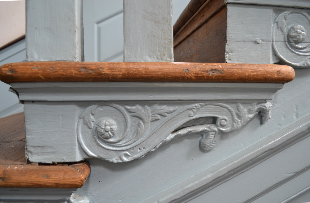 Detail showing side view of scroll and leaf brackets underneath a stair tread.