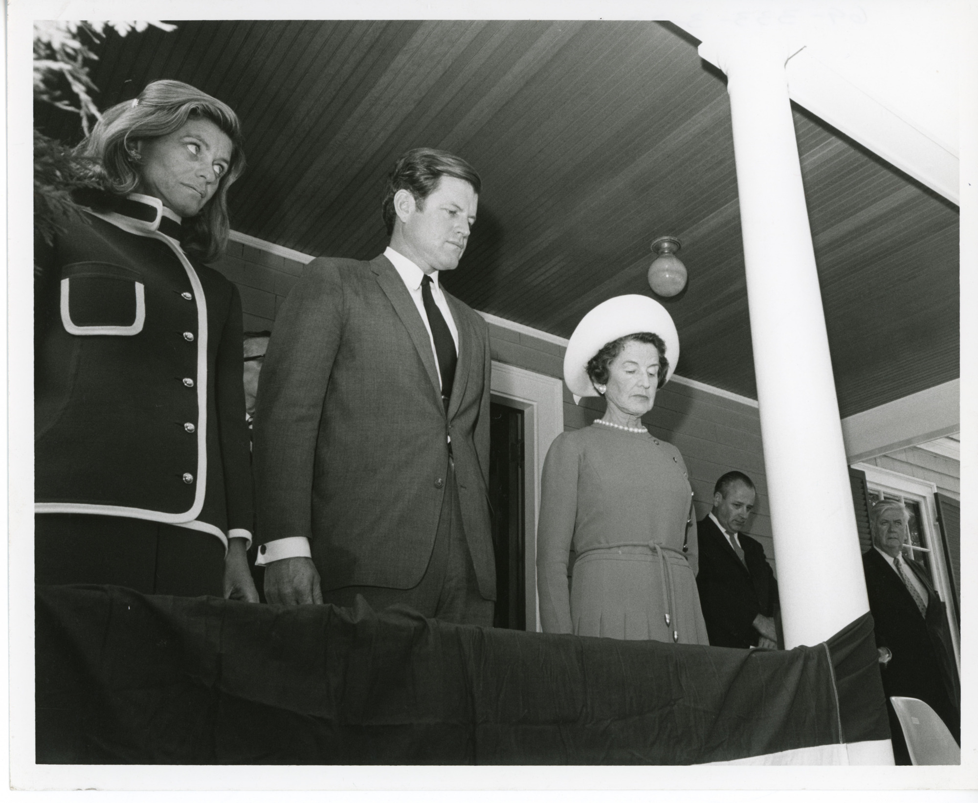 Three people with bowed heads stand on porch