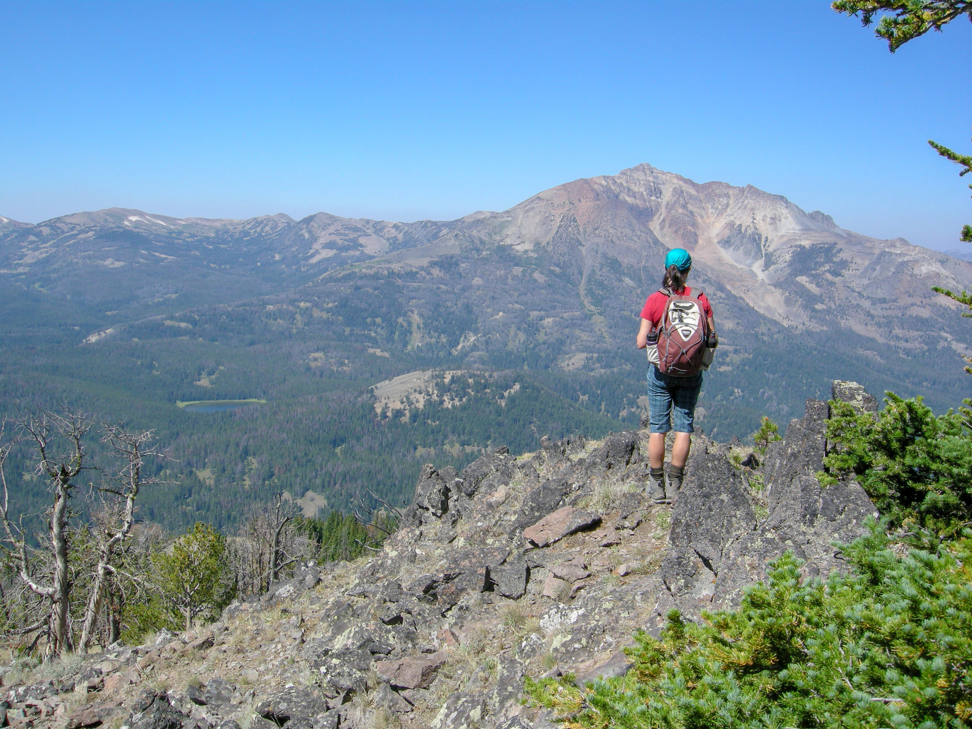 One woman hiker standing on the highest point of a rocky ridge looking ahead at a large mountain.