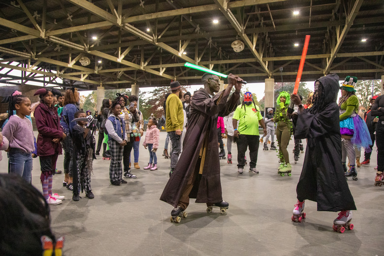 Two people dressed up as jedi from Star Wars pretend to have a sword fight as a group surrounds them