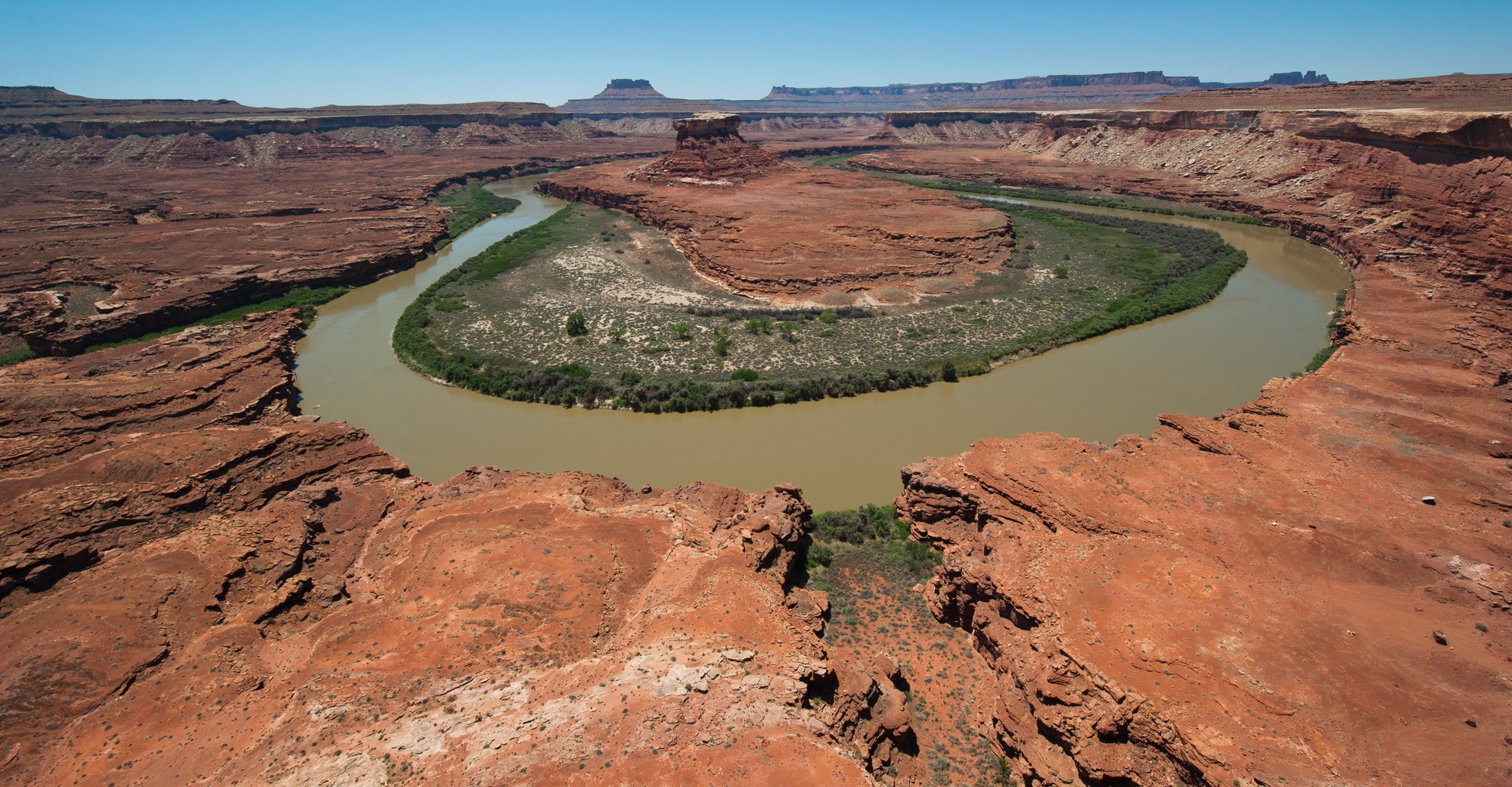 a greenish brown river flows in the shape of a horseshoe through a canyon of reddish rocks 
