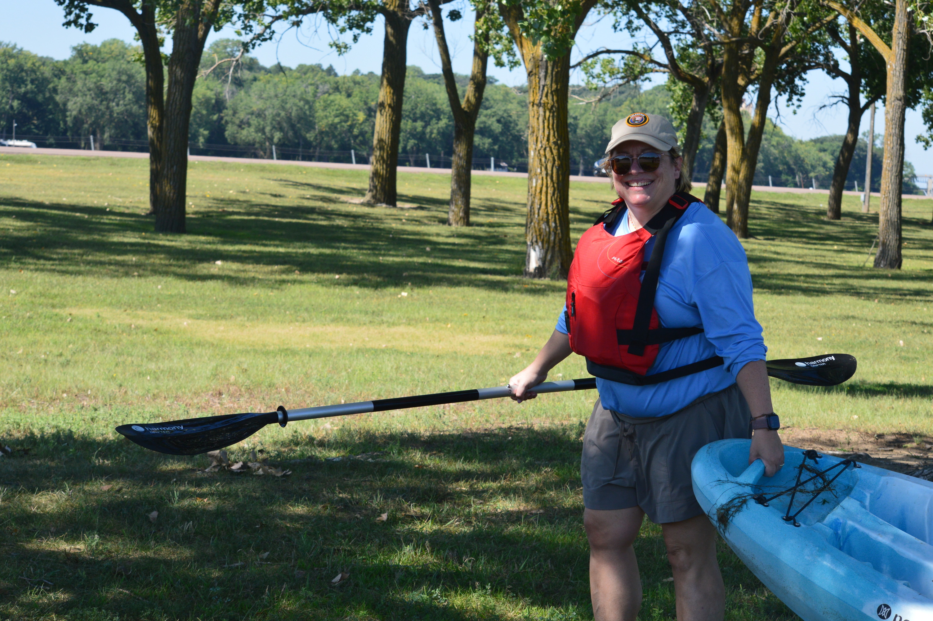 A woman wearing a life jacket holds a paddle in one hand and pulls the end of a kayak with the other. 