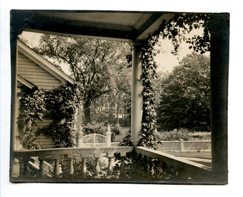 Black and white photograph of view off porch, with garden in distance.