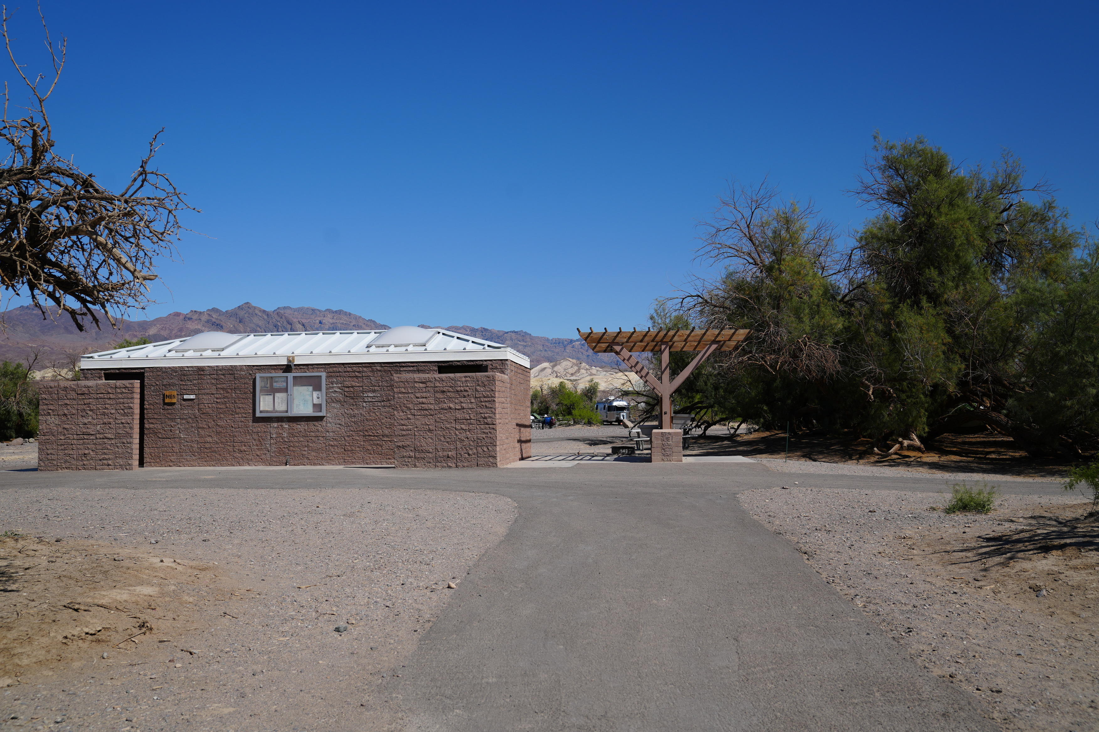 Furnace Creek campground restrooms closest to ADA sites 135 and 148. Brick restroom building with asphalt path leading to concrete entryway. To the right there's a sink with shade.