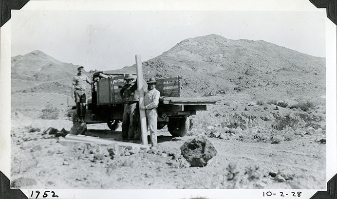 This is an historic black and white photograph from the Scotty's Castle Historic Photograph Collection, Death Valley National Park of three unidentified men with truck installing concrete fence posts, unknown location at Death Valley Ranch. October 2, 1928.  Photographed by Mat Roy Thompson.