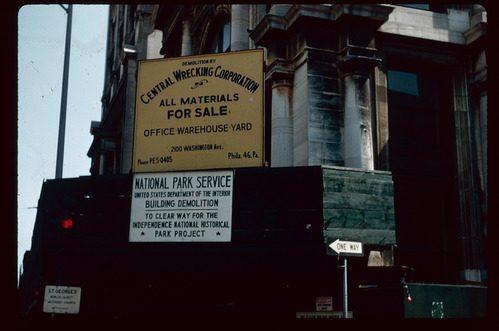 Yellow materials sign above a National Park Service demolition sign on a building.
