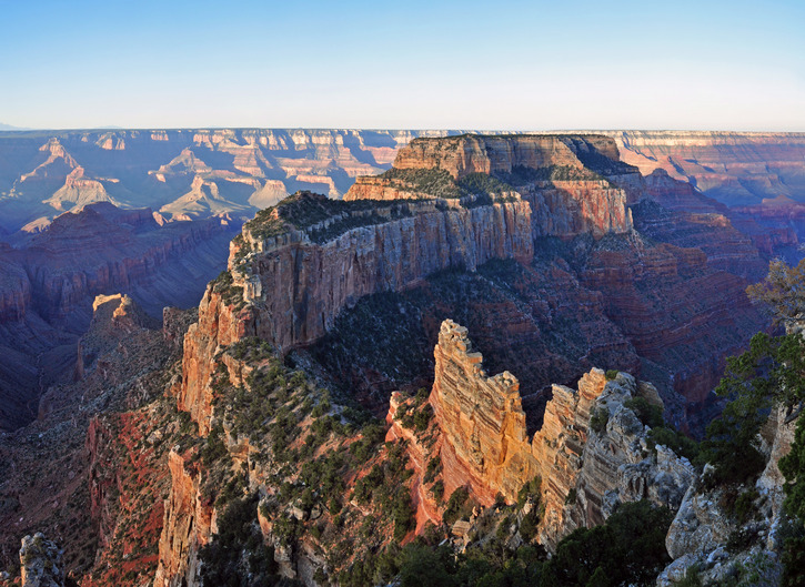 Photograph of the sunrise from Cape Royal, North Rim, Grand Canyon National Park. Low light illuminates horizontal layers of rock in shades of red and white.