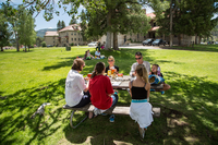A family of six sits at a picnic table on a grassy lawn with Fort Yellowstone in the background.