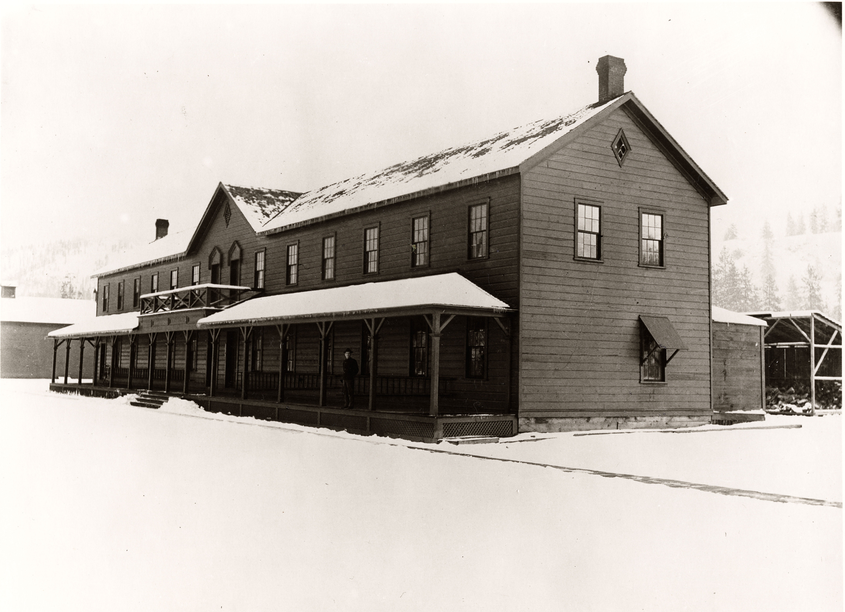 Black and white photograph of multistory long wooden building covered in snow