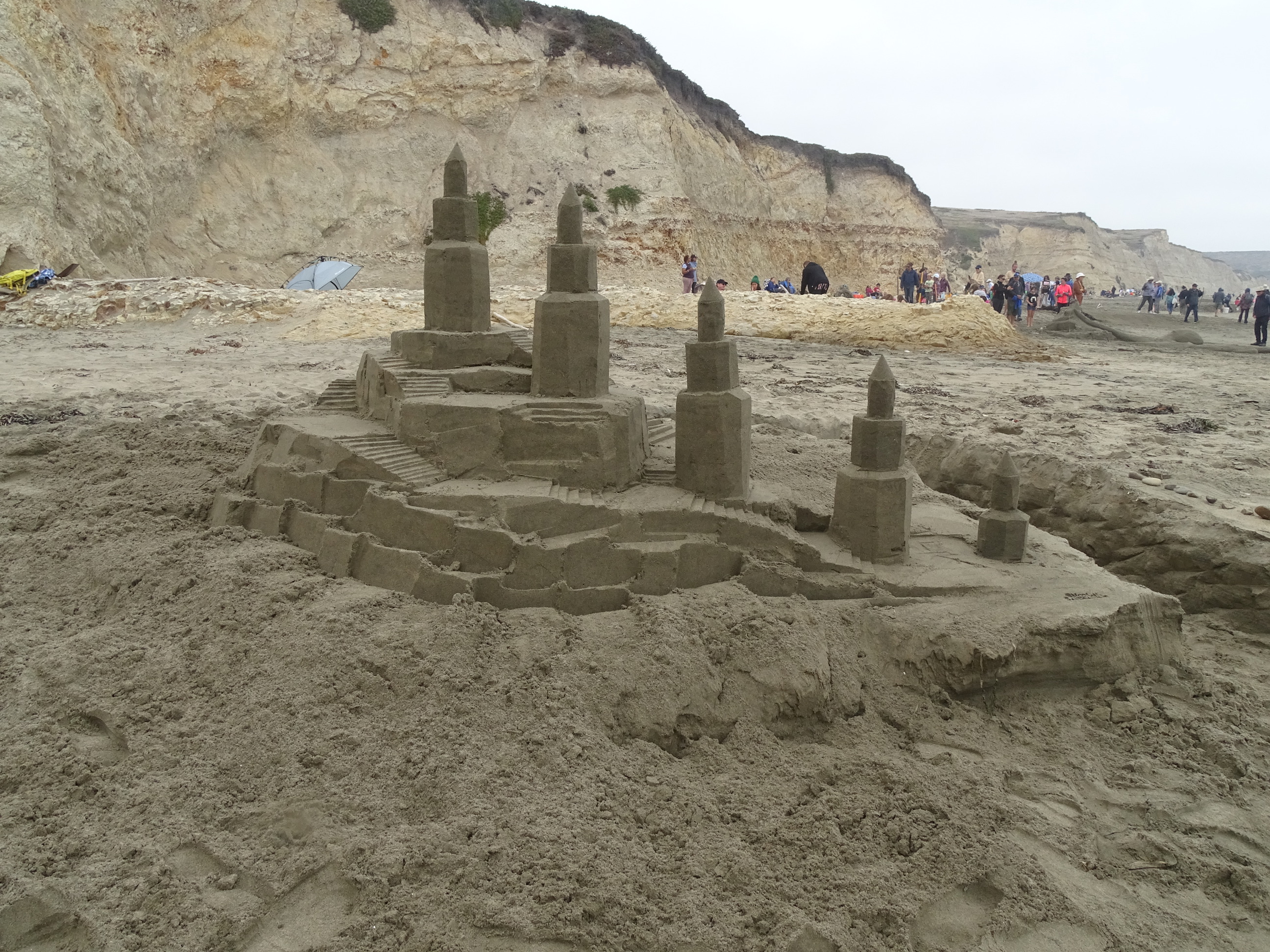 A large sand sculpture of a castle with five octagonally shaped towers and lots of staircases.