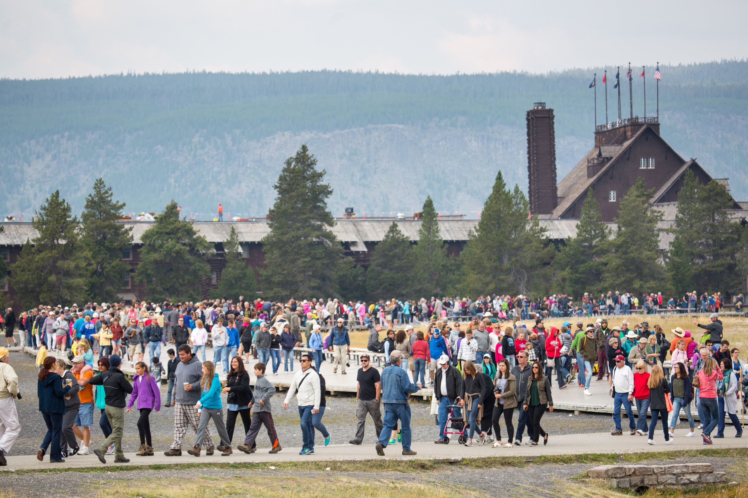 Hundreds of people walking on the boardwalk with Old Faithful Inn in the background.