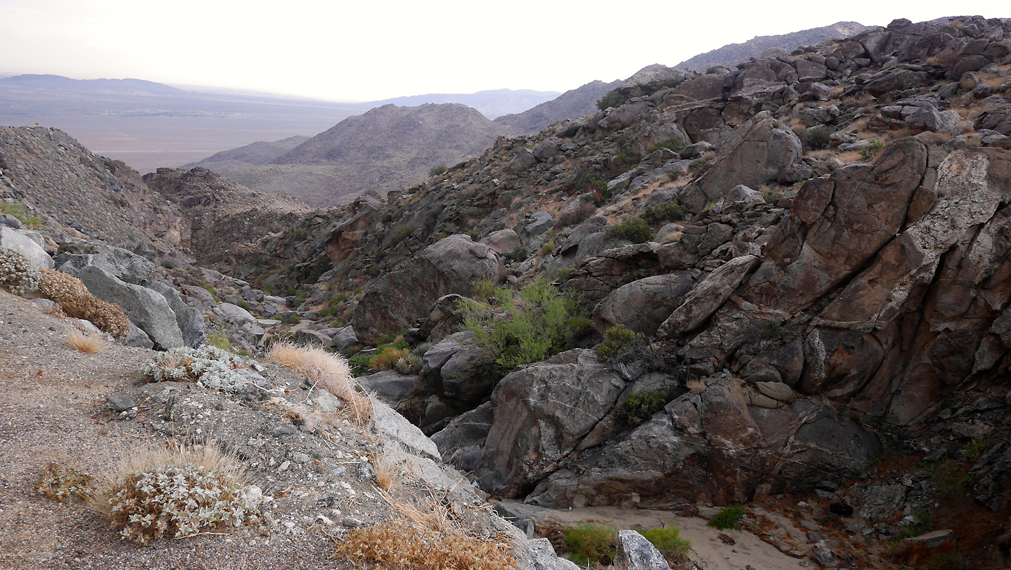 A valley between two mountains with large rocky boulders and desert scrub