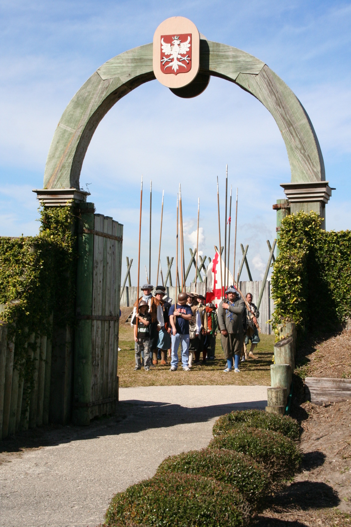Visitors and reenactors in costume carry pikes to the fort gate 