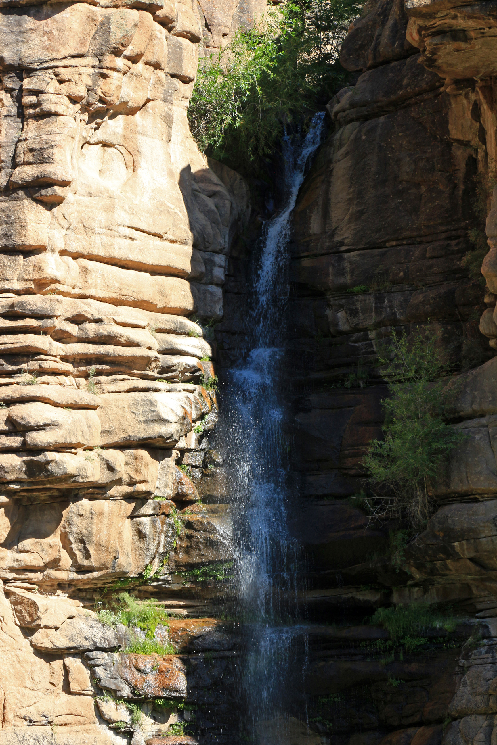 A small waterfall is hidden in shadows between canyon walls
