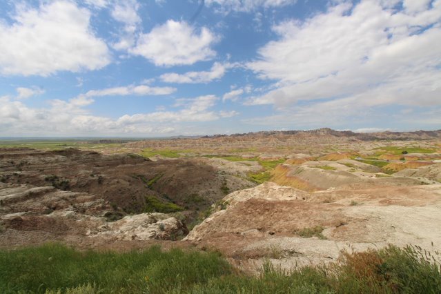 yellow, red, and brown buttes leading down to a grassy valley with higher buttes on the horizon