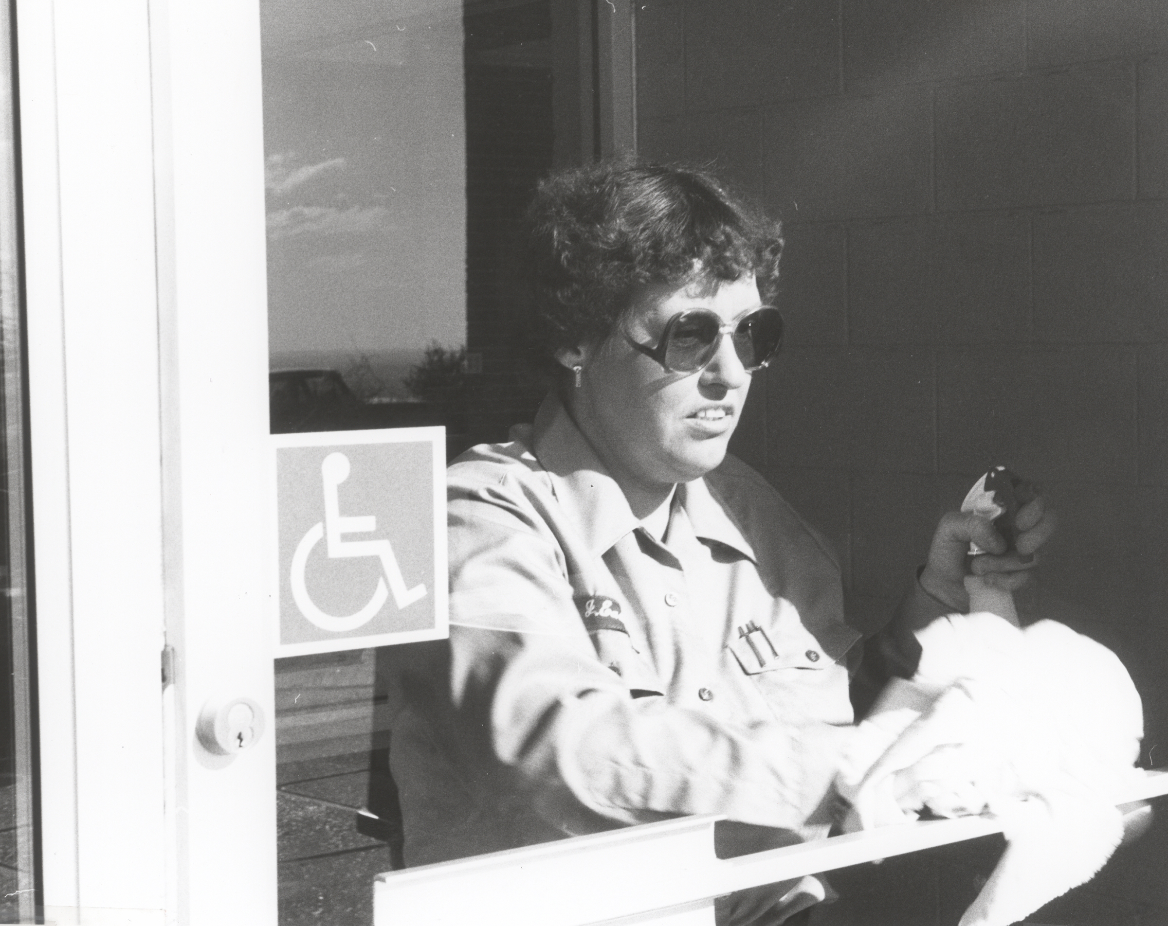 Joan Easley in her NPS uniform cleans a glass door with a rag and liquid in a spray bottle. 